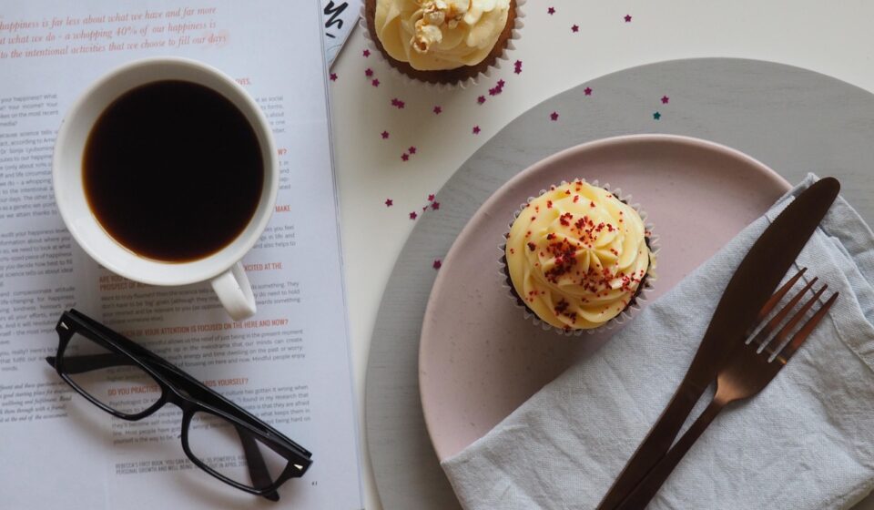 coffee, cup, drink, breakfast, food, chocolate, sweet, table, sugar, espresso, spoon, plate, tea, hot, mug, saucer, coffee cup, glasses, desktop, table top, cupcake, cake, icing, dessert, table wear, magazine, read, cafe, caffeine, cappuccino, white, black, beverage, tea cup, morning